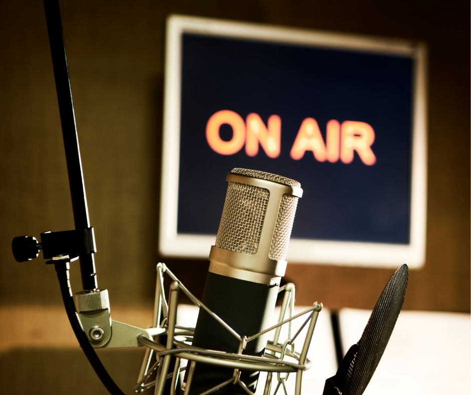 A close up of a microphone with an "on air" sign in the background conveying media being created