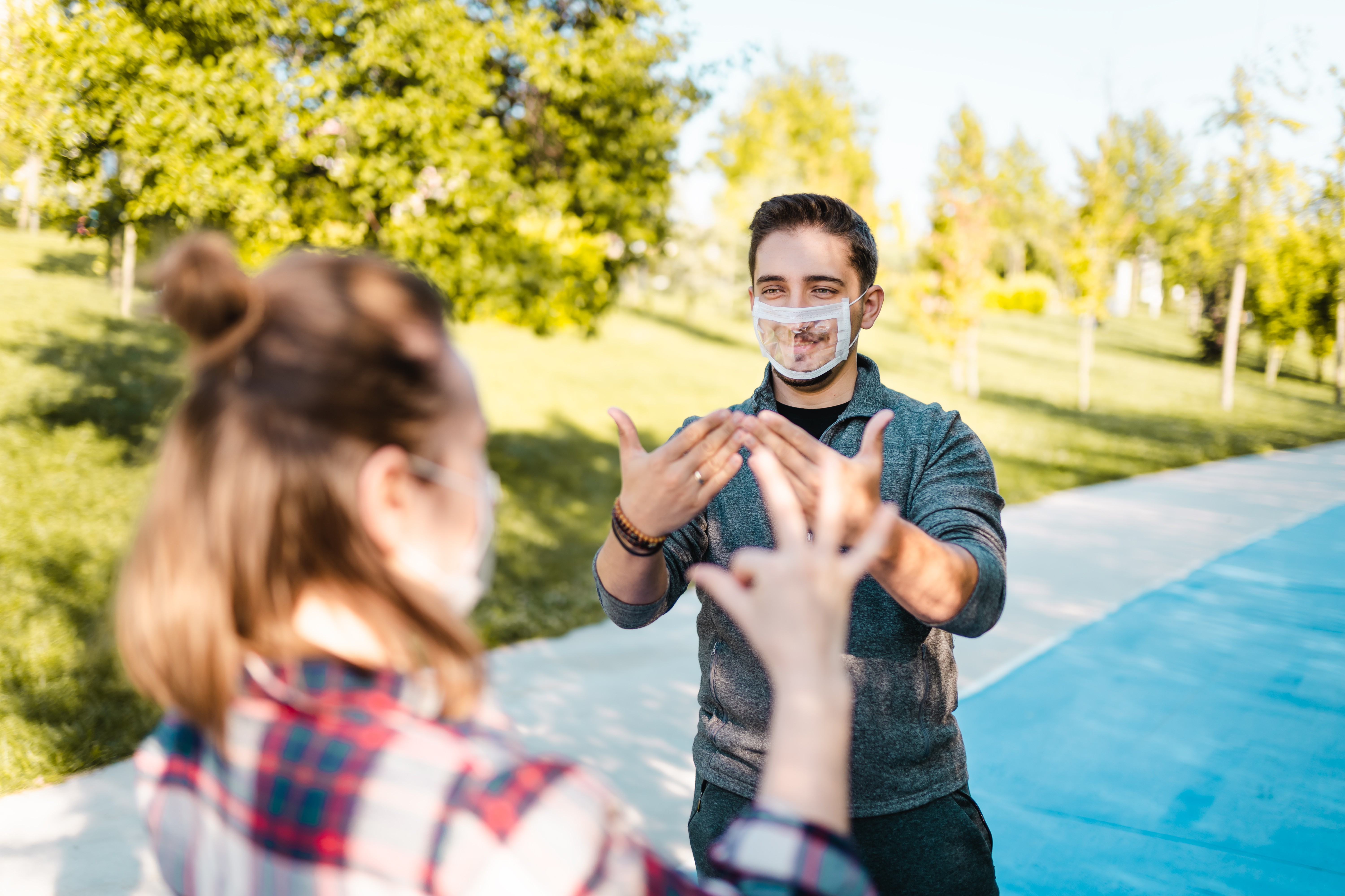 Two people standing outside communicating through sign language with a clear mask on the face