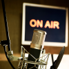 A close up of a microphone with an "on air" sign in the background conveying media being created